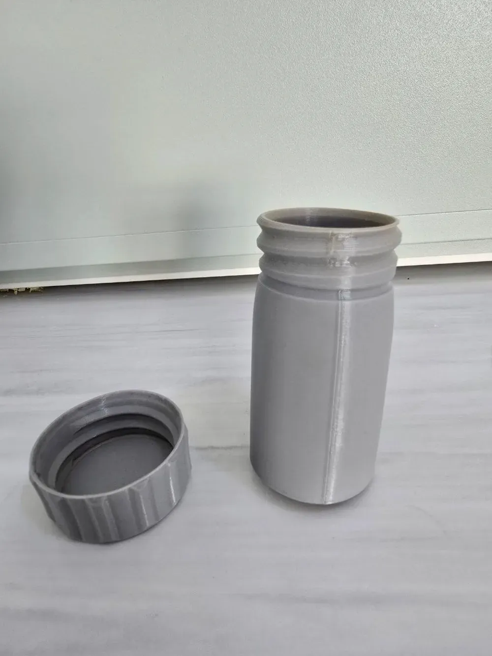 A grey 3D-printed PETG container with the lid off, its opening warped out of round after an afternoon in a hot car